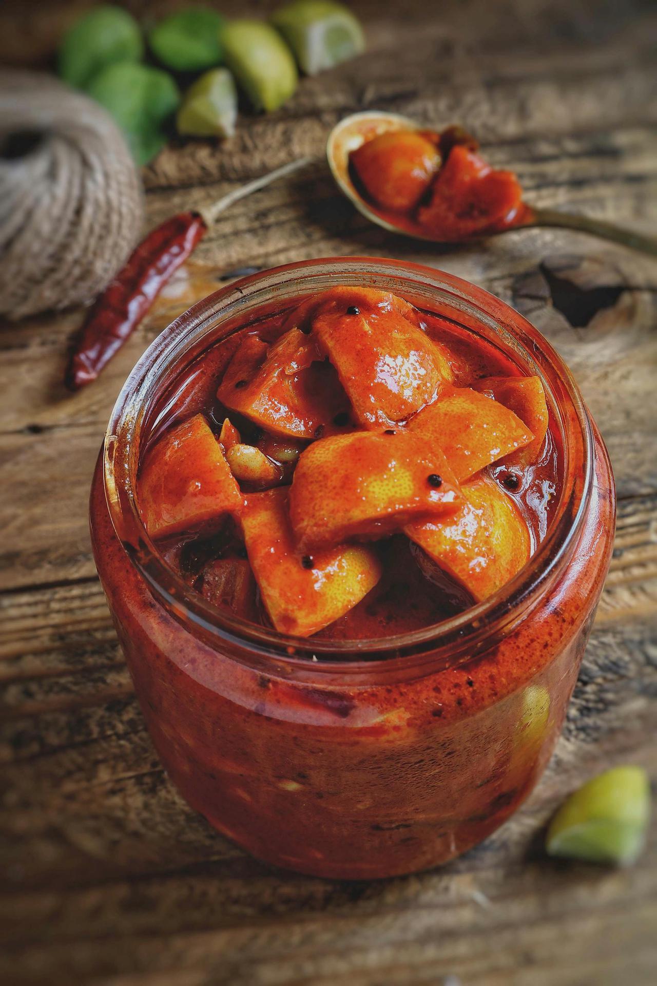 Delicious homemade mango pickle in a jar with spices on a wooden table.